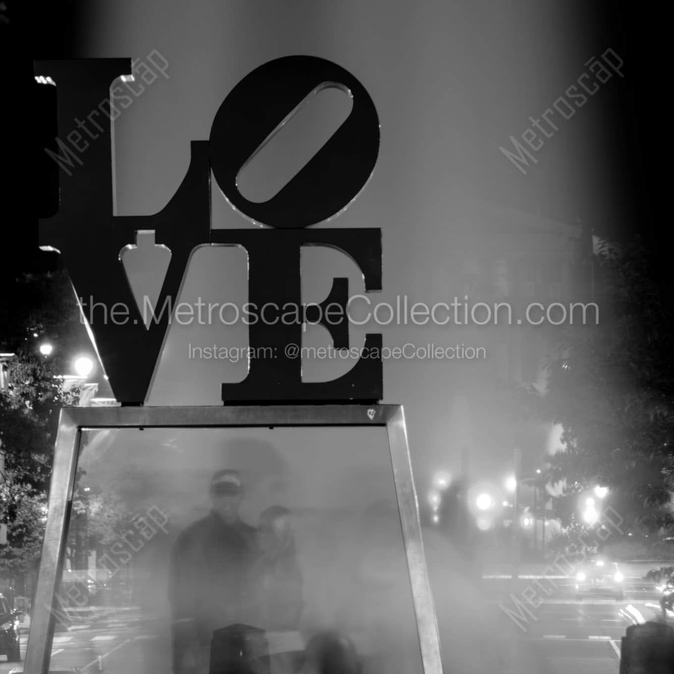 couples pose under love sculpture Black & White Wall Art